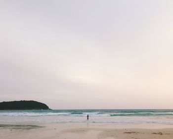 Rear view of woman standing at beach against sky