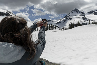 Unrecognizable female traveler using compass for navigation during trip through snowy mountains on cloudy spring day