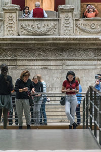 Full length of young woman using mobile phone on staircase