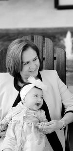 Mother with cute daughter sitting on chair against sky