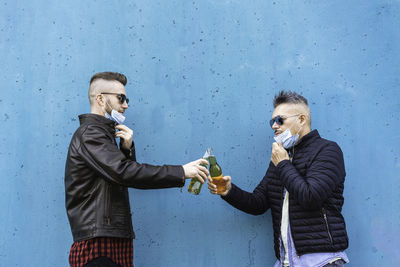 Men wearing mask holding beer standing against wall outdoors