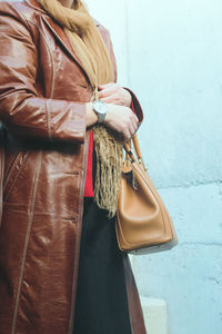 Midsection of woman wearing leather overcoat standing against wall