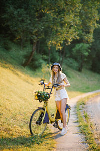A young beautiful woman holds a bicycle with yellow verbena flowers in a basket on an outdoor