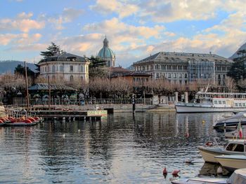 Boats moored in river by buildings against sky