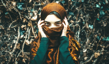 Portrait of young woman covering face with scarf
