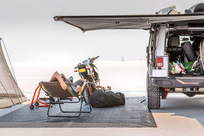 Man relaxing on chair by car at beach