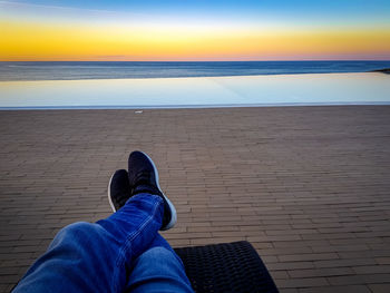 Low section of man relaxing by sea against sky