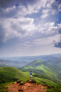 Rear view of man standing on mountain against cloudy sky