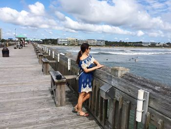 Young woman standing on bridge by sea against sky