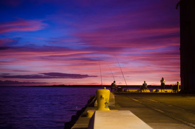 Rear view of people at harbor by sea against sky during sunset