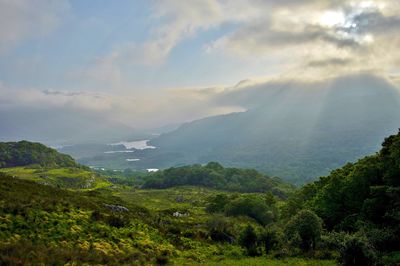 Scenic view of green mountains against cloudy sky during sunny day