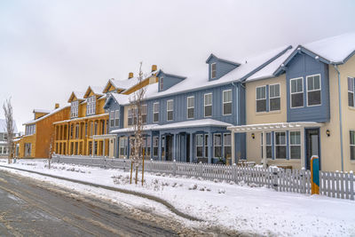 Snow covered road by buildings against sky