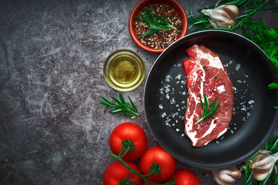 Raw beef steak with tomato, garlic, pepper, salt and rosemary on frying pan on a dark background.