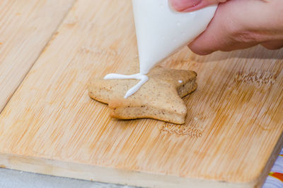 Cropped hand icing gingerbread cookie on cutting board during christmas