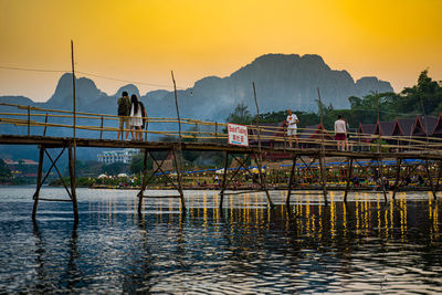 People on lake against sky during sunset