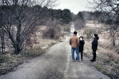 Rear view of men walking on footpath amidst bare trees