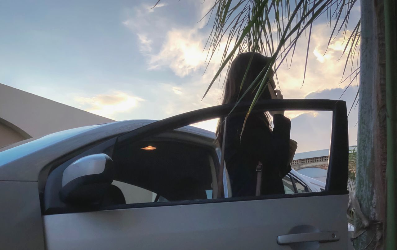 WOMAN SEEN THROUGH CAR WINDOW AGAINST SKY