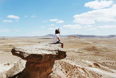 Man sitting on rock at beach against sky