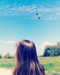 Rear view of woman flying over field against sky