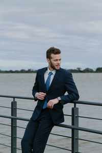 Young man standing by railing against sea