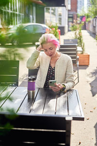 Alternative female with short hair browsing social media on smartphone while sitting at table in street cafe on sunny day