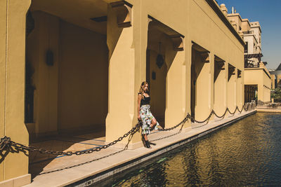 Mid adult woman standing by canal amidst building