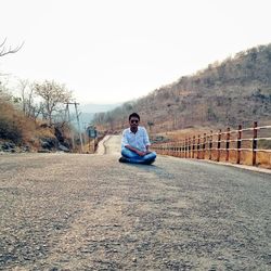 Portrait of young man sitting on wall against sky