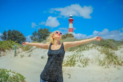 Woman with arms outstretched standing against lighthouse