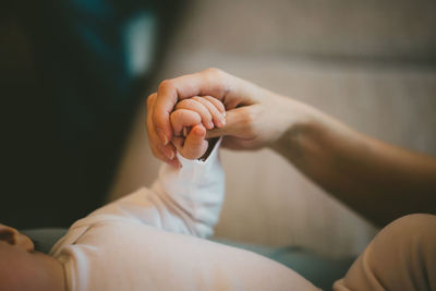 Cropped image of mother holding toddler hand at home