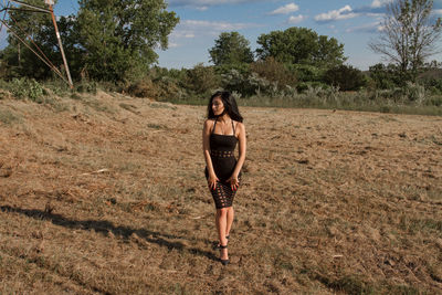 Young woman standing on field against trees