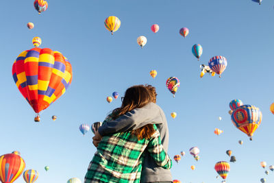 Low angle view of couple embracing against hot air balloons in sky