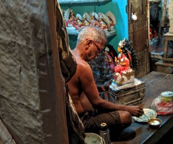 Shirtless man working on sculpture at workshop