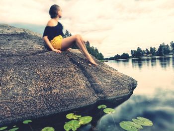 Woman sitting on rock by sea against sky
