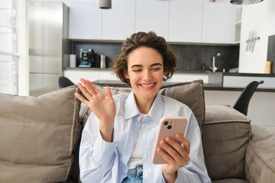 Young woman using phone while sitting on sofa at home