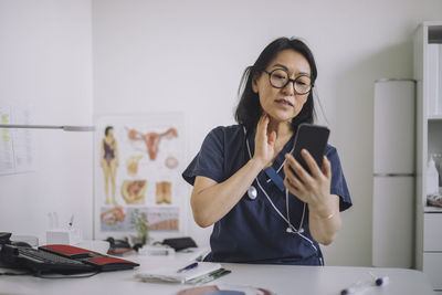 Female otolaryngologist doing online consultation through mobile phone while sitting at desk in medical clinic