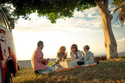 Group of people sitting on grassland against the sky