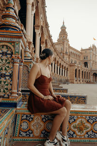 A young woman sitting in front of a historic building - plaza de espana. spanish square
