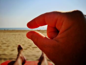 Close-up of hands on beach against clear sky