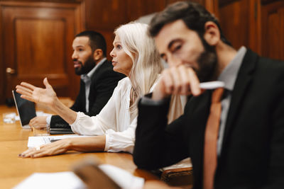 Confident businesswoman gesturing while discussing strategy amidst male colleagues in board room