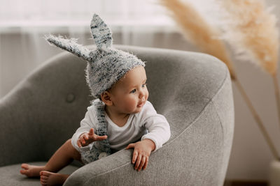 Cute baby wearing bunny cap looking away while sitting on sofa