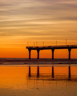 Silhouette bridge over sea against orange sky