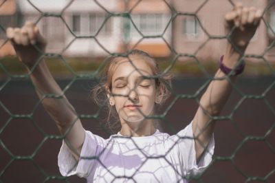 Portrait of a teenage girl looking through chainlink fence
