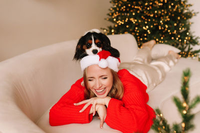 A happy cheerful girl in a sweater and a santa hat plays and cuddles with a pet dog 