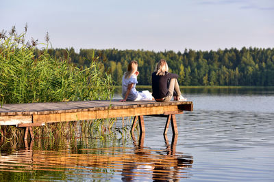 People sitting by lake against sky