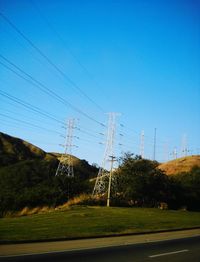 Electricity pylons on field against blue sky