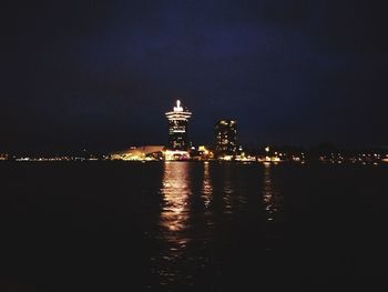 Illuminated buildings by sea against sky at night