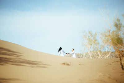 Mid distance view of couple holding hands at desert against blue sky