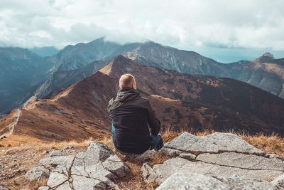 Rear view of man sitting on rock