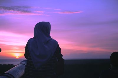 Rear view of woman in hijab sitting against sky during sunset