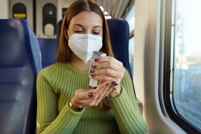 Business woman with medical face mask using alcohol gel sanitizing hands on public transport